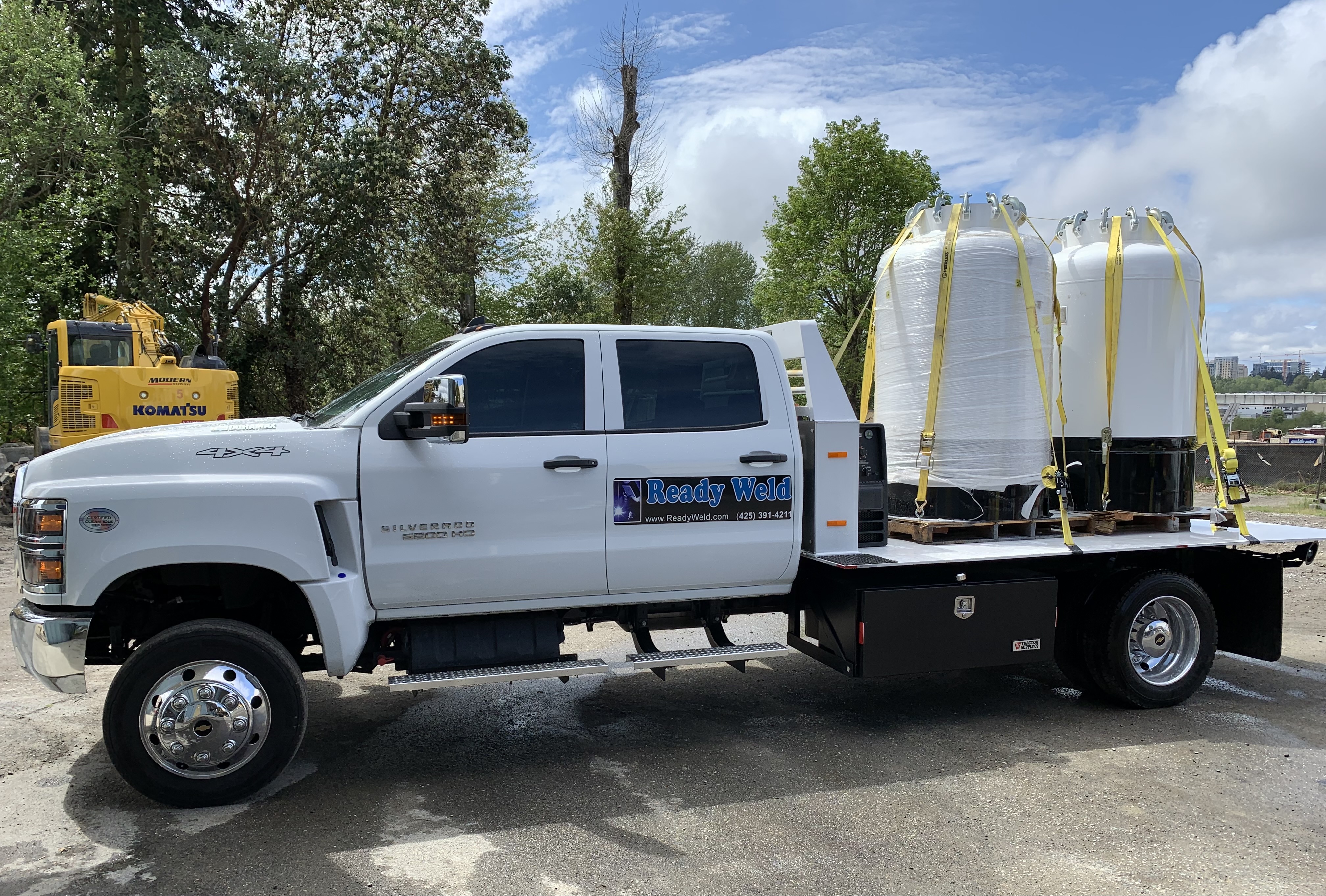 White ReadyWeld truck with large white tanks on flatbed, parked near trees