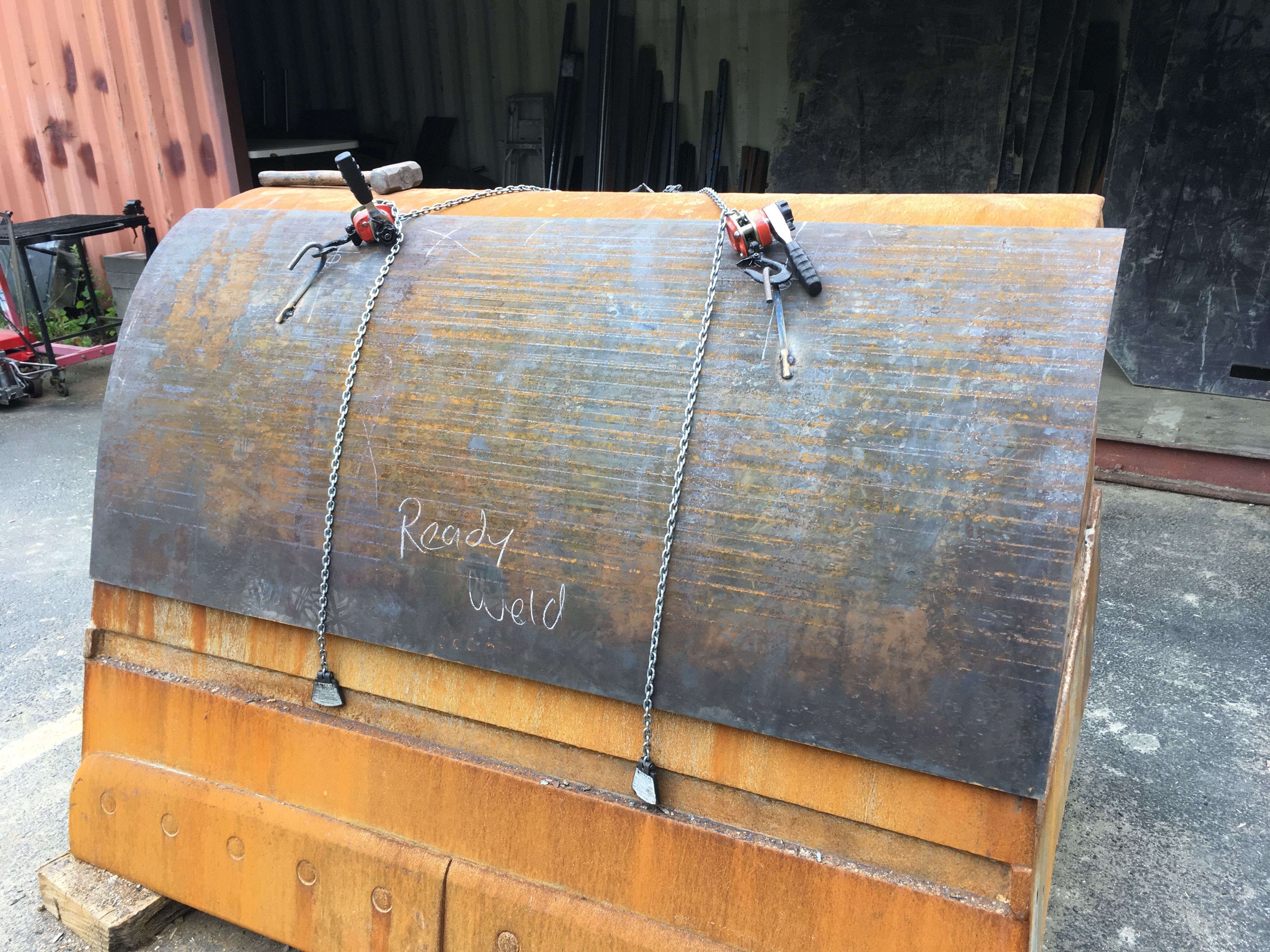 Rusty metal sheet secured with chains, marked "Ready Weld" in workshop