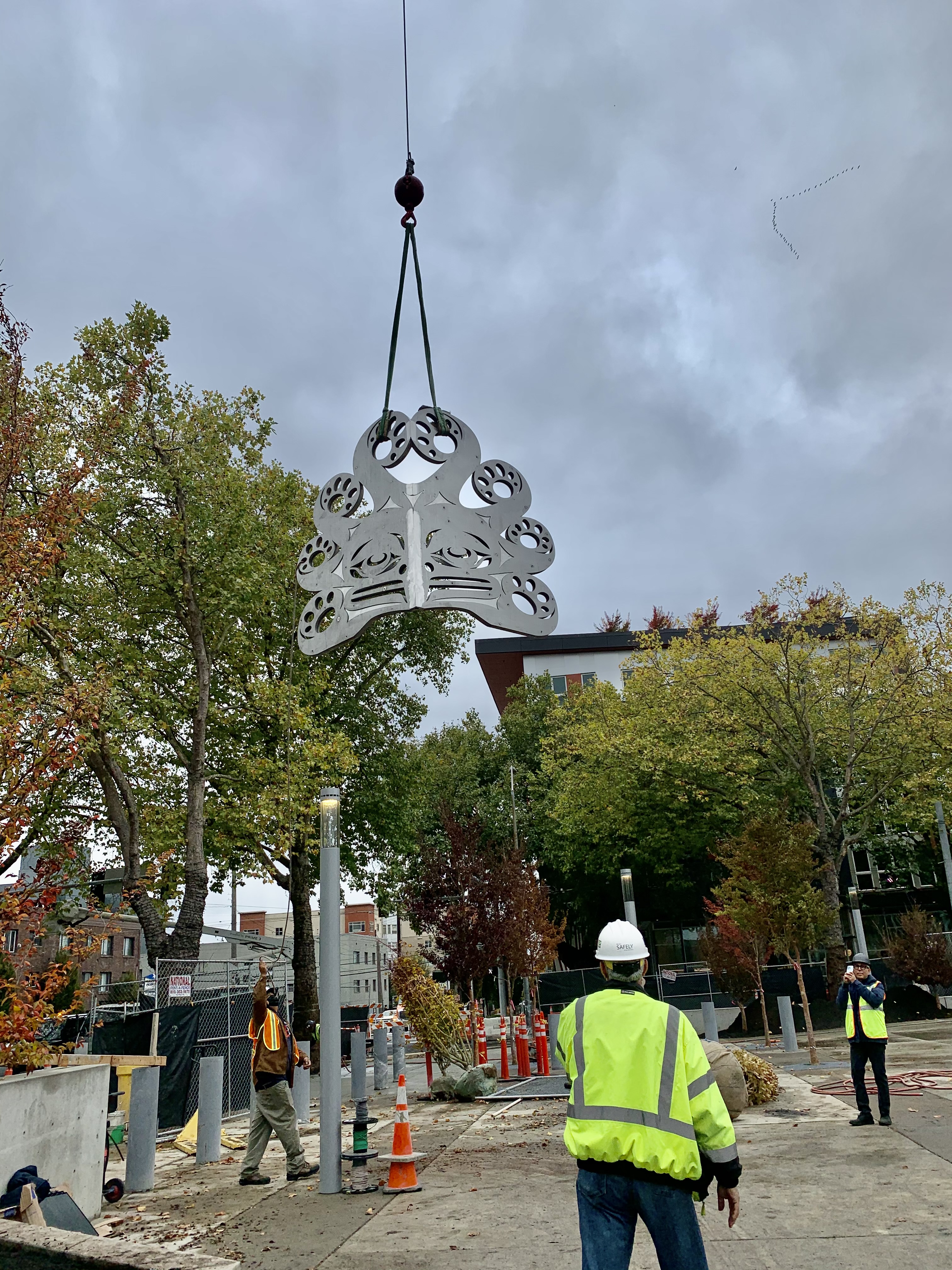 Large metal sculpture being installed by construction workers on urban street