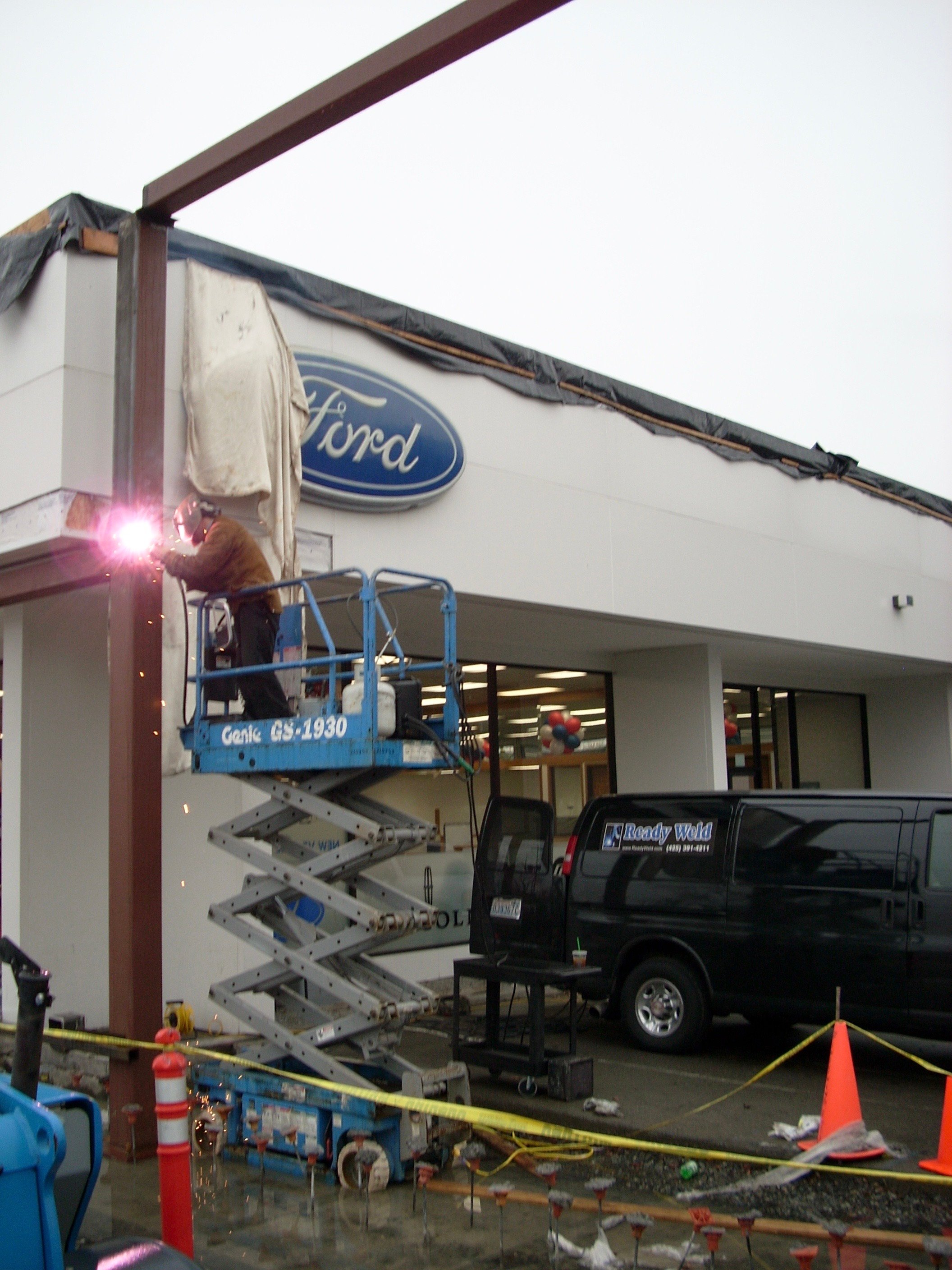 Welder on scissor lift repairing Ford dealership building exterior